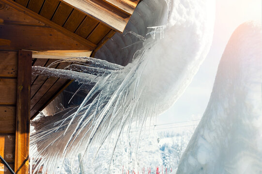 Close-up detail view of melting snow icicles on wooden alpine hut roof at windy mountain. Beatiful croocked big icicles on cold frosty sunny winter day