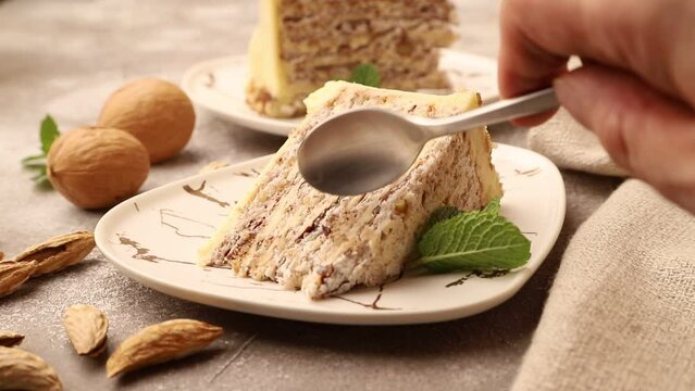 Homemade walnut and almond cake is cut with a spoon on a ceramic plate on brown concrete background. Side view, close up.