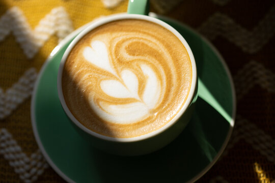 Cappuccino with latte art in a green cup in hard light. Close up.