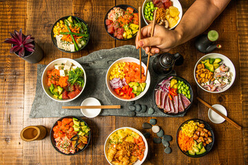 A person's arm with chopsticks among a pile of bowls of fresh and healthy food