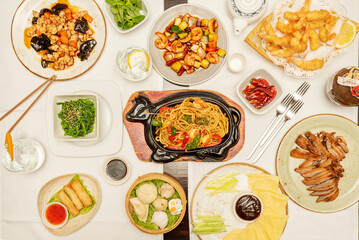 Fototapeta na wymiar Set of mainly Asian and Chinese dishes, udon noodles with vegetables and shrimp, Vietnamese rolls, chicken with shiitake mushrooms, spicy shrimp with vegetables, and shrimp tempura