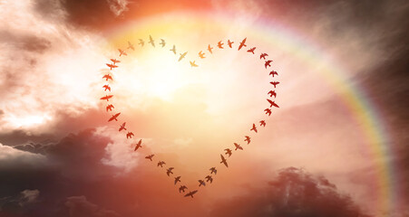Lecące ptaki w kształcie serca na rozświetlonym niebie - obrazy, fototapety, plakaty