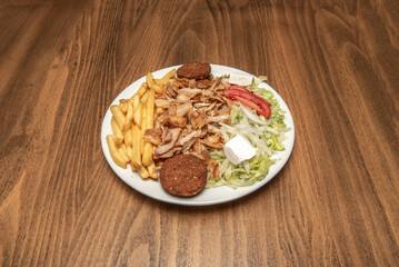 Kebab menu plate with big pile of chicken and lamb meat with salad and french fries, falafel, white onion and fresh cheese