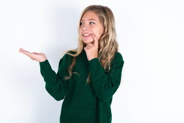 Obraz premium Positive beautiful caucasian teen girl wearing green knitted sweater over white wall advert promo touch finger teeth