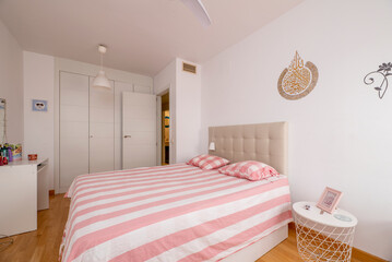 Bedroom with double bed with pink and white striped duvet, white furniture and cabinets and decorations