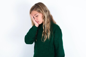 beautiful caucasian teen girl wearing green knitted sweater over white wall with sad expression...