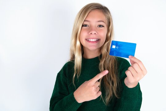 Photo portrait of beautiful caucasian teen girl wearing green knitted sweater over white wall doing purchase with pointing finger credit bank card