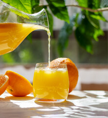 Orange juice pouring from pitcher into glass. Healthy citrus drink. Summer freshness concept.