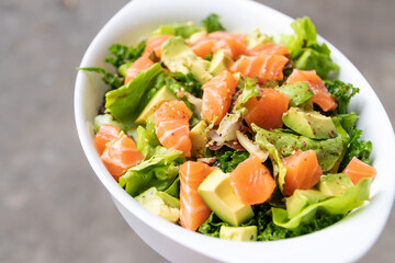 Salmon salad with green leaves and avocado on oval white bowl.