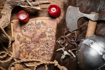 Ancient map, battle axe, viking axe and burning candles on the top view table background.