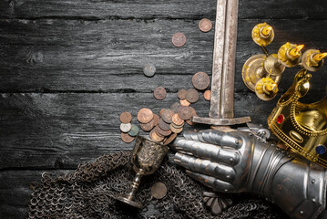 Knight sword, golden crown and armor mitten on the black woorden flat lay table background with...