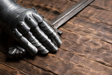Knight sword and steel gloves on the wooden table close up background with copy space.