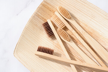 Many bamboo toothbrushes with natural bristle on wooden tray over white marble table background....