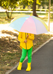 Little cute girl kid child in a yellow raincoat with multicolored rainbow umbrella