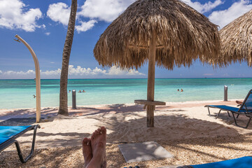 View of feet of man on sunbeds on sandy beach. Gorgeous turquoise water surface of Caribbean sea on background. Aruba.