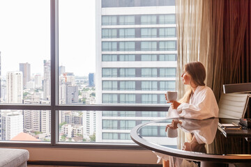 Woman in bathrobe with coffee cup sitting in modern hotel or apartment
