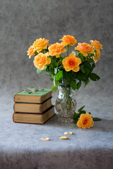 Bouquet of cream roses in a crystal vase, three books and glasses on grey background