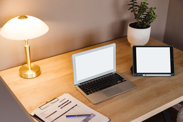 Modern workplace with laptop and tablet with white blank screen.