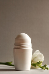 White roll-on antiperspirant deodorant bottle on a gray background with freesia branch. Skin care concept. Copy space.