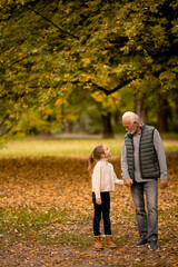 Grandfather spending time with his granddaughter in park on autumn day