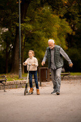 Senior man teaching his granddaughter how to ride kick scooter in park