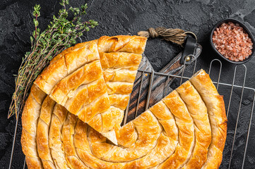 Turkish Tepsi Boregi, Round Borek cheese pie on kitchen board. Black background. Top view