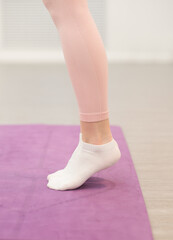 woman legs wearing leggings and sport socks standing on yoga mat. woman stands on tiptoe doing exercises, vertical crop view.