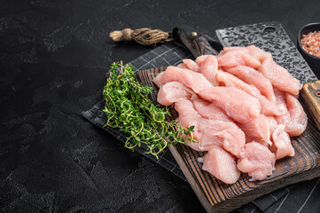 Fresh Raw turkey breast meat slices on a butcher board. Black background. Top view. Copy space