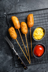 Deep fried corn dogs with mustard and ketchup. Black background. Top view