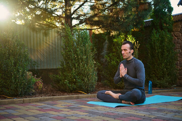 Sunset sunlight fall on the backyard, while a handsome active man, yogi meditating in lotus...
