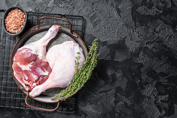 Raw Free range duck legs in a steel tray with thyme. Black background. Top view. Copy space