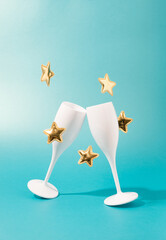 Champagne glasses clashing with golden stars falling against the teal background. New Year, Christmas celebration template.