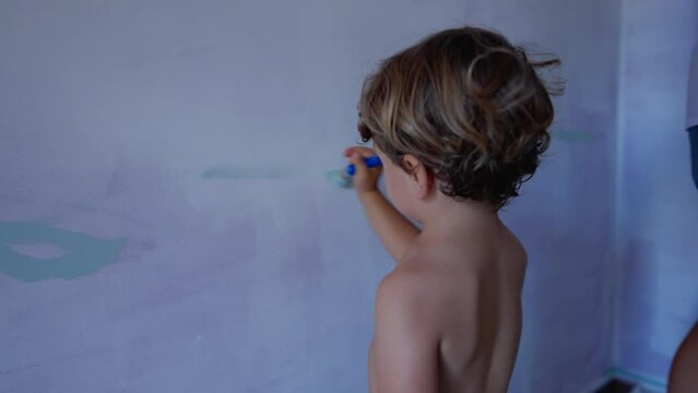 Child painting wall with paint brush. One little mischievous kid paints apartment wall