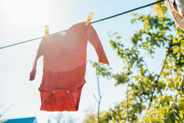 Baby bodysuits for a newborn are hung on a rope with clothespins on a background of blue sky and leaves