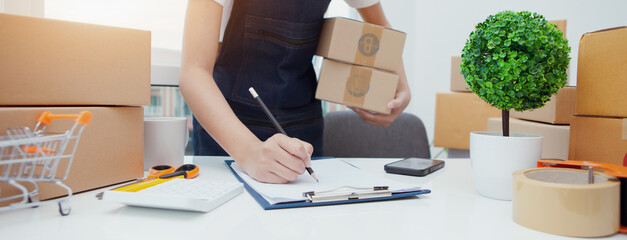 Asian woman business owner with many parcel boxes on table Happy with online sales, use smartphone,...