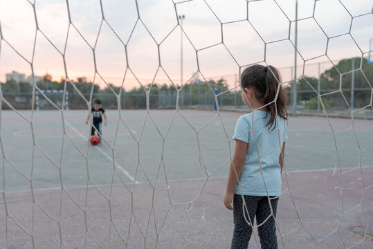 Back view of child goalkeeper ready to catch a soccer ball stand on soccer field in football goal. Selective focus on girl.