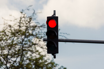 Red light on semaphore with a tree and cloudy sky in the background