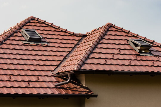 Brown tiles on the roof of a new home with attic windows open for ventilation