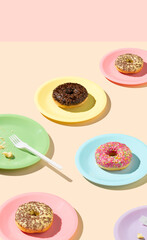 Creative pattern of colored plates with vanilla, chocolate and fruit donuts. Party concept on pastel beige table and pink background.