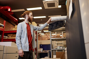 Side view portrait of young man taking out vinyl roll in industrial printing shop