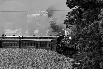 View of a Restored Steam Passenger Train Approaching Around a Curve With Smoke and Steam in Black and White