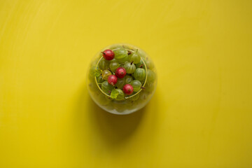 Gooseberries in a transparent jar on a yellow background