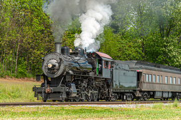 Fototapeta na wymiar View of an Antique Restored Steam Passenger Train Approaching Along a Lone Rail Road Track on a Spring Day
