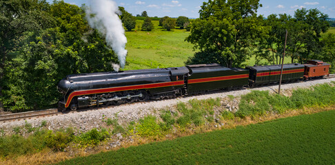 Drone View of an Antique Steam Engine, Blowing Steam and Traveling Along the Countryside Pulling a Caboose on a Sunny Day © Greg Kelton