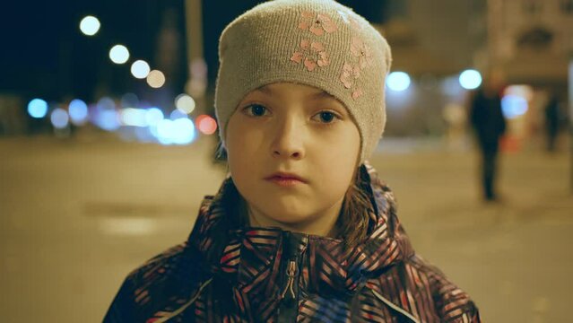 Lonely Sad Little Girl Standing In Street In Night Dark City With Passed By Cars And Walking Pedestrians. Problems Of Parenting. Concept Of Solving Psychological Factors