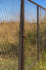 A closed gate in a chain-link fence in a field. Close-up.