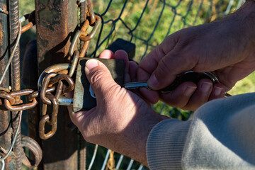 Close-up of a man's hands opening the lock in the gate.