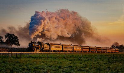 A View of an Antique Steam Passenger Train Approaching at Sunrise With a Full Head of Steam and Smoke Traveling Thru Farmlands - obrazy, fototapety, plakaty