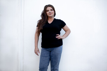 Beautiful plump woman wearing jeans and t-shirt posing against the street wall in the city