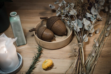 Dark brown acrons made of wood on a table with dried plants next to them